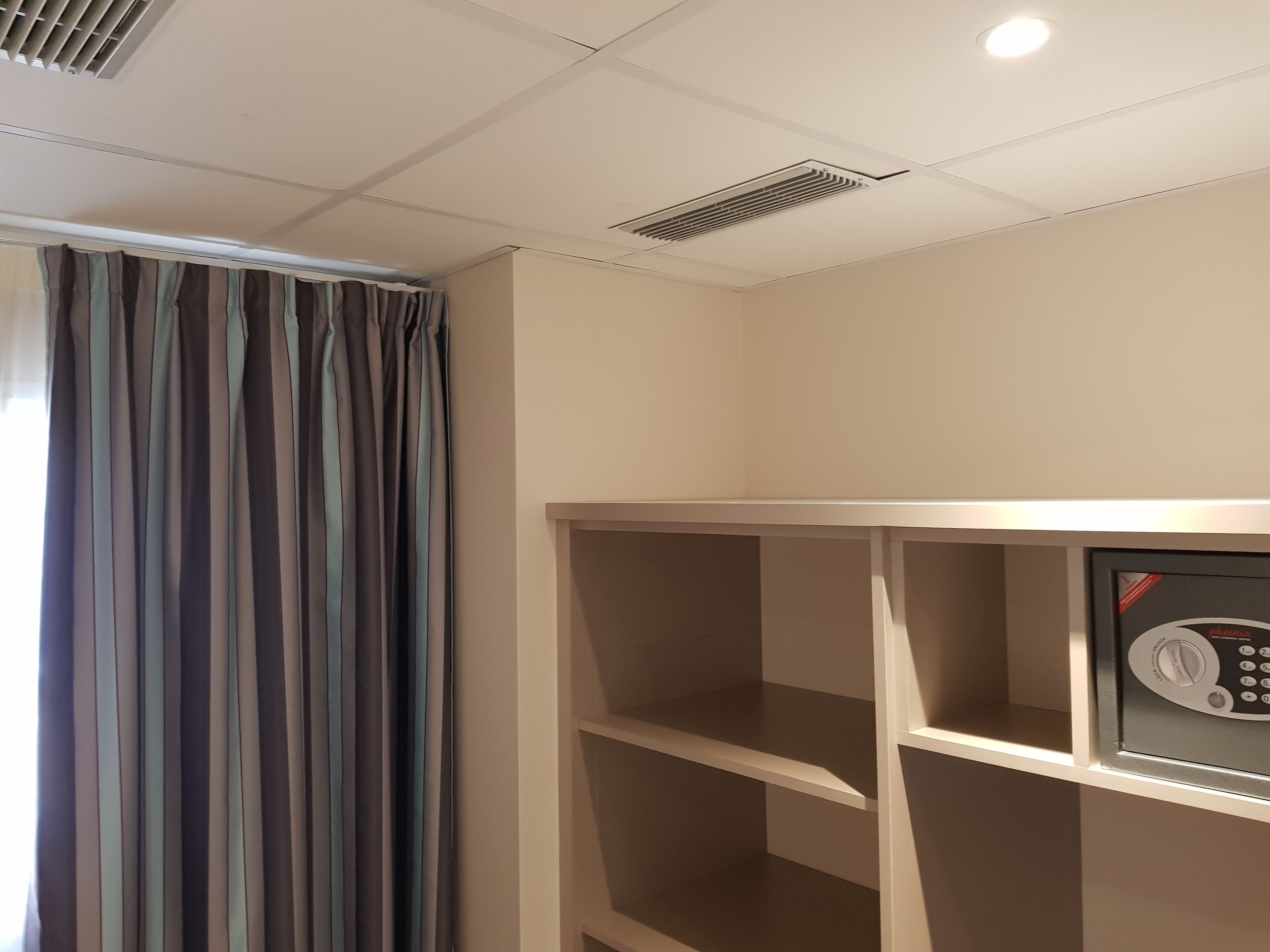 A hotel room with a large window, a built-in telephone, and a ceiling vent.