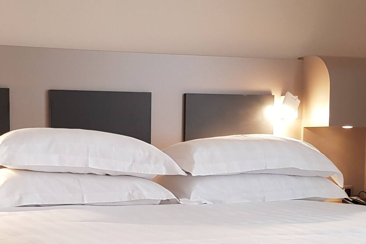 A hotel room with a large bed, two bedside lamps, and a wall-mounted light fixture.