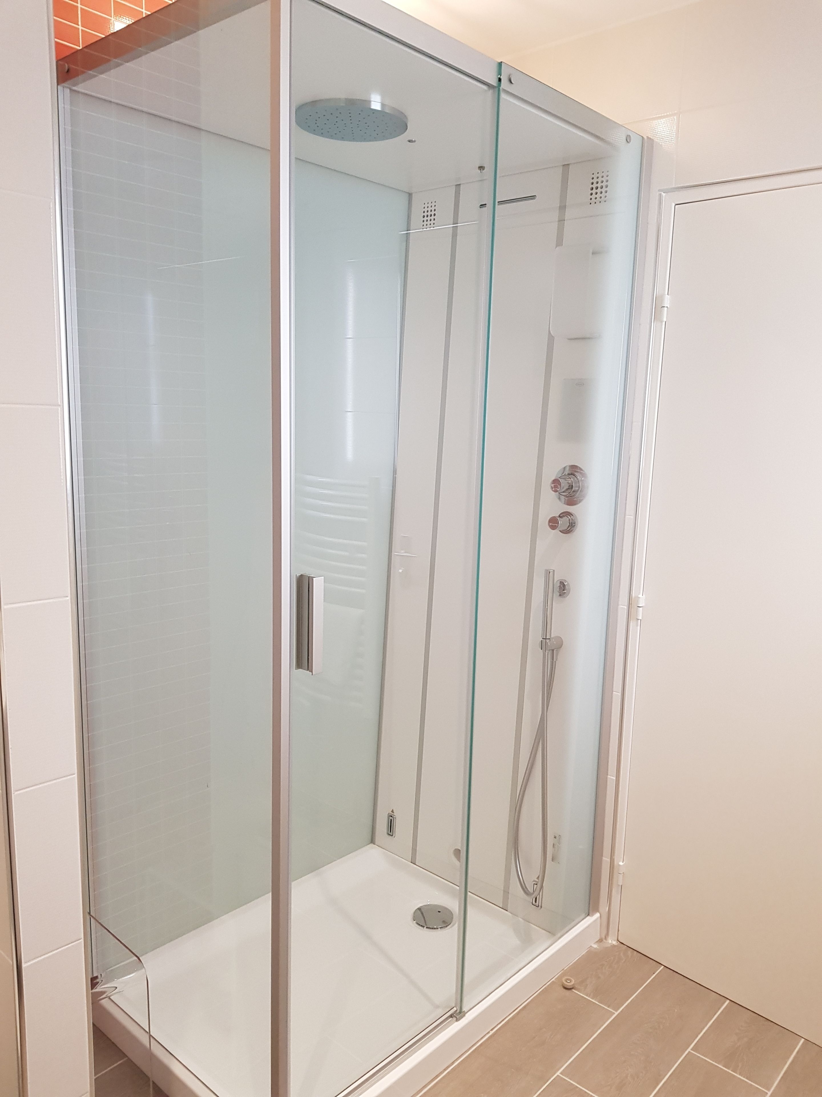 Une cabine de douche entièrement vitrée, avec un sol blanc et une porte en verre.