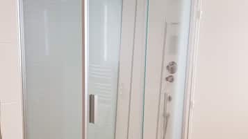 Une cabine de douche entièrement vitrée, avec un sol blanc et une porte en verre.