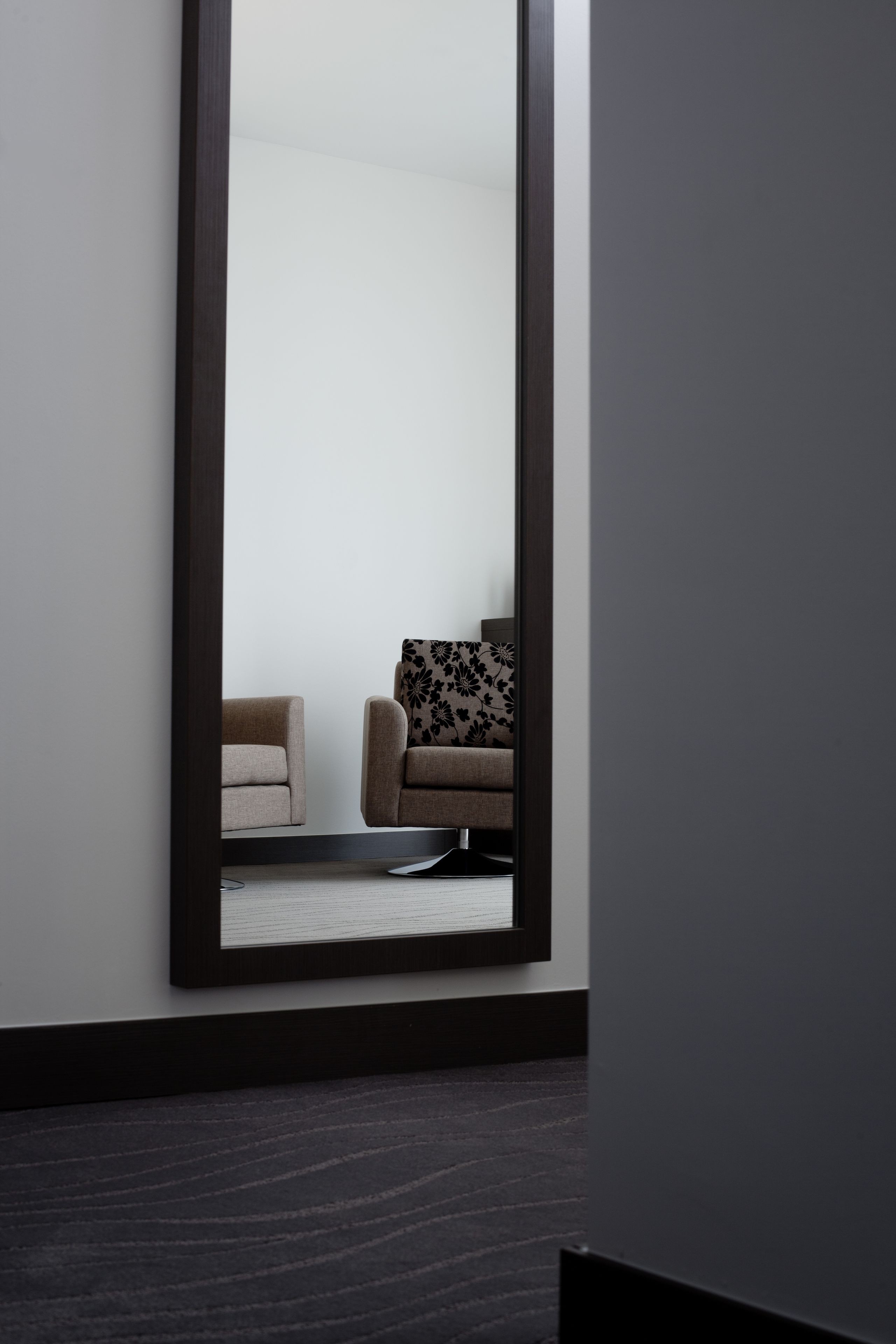 A modern room with a large mirror reflecting a sofa and a patterned pillow.