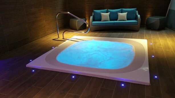 A modern spa area with a heated floor, a massage chair, and a blue-lit hot tub. - Brit Hotel de Grignan (Vichy)
