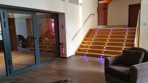 A modern interior with a staircase, a glass door entrance, and a wicker chair. - Brit Hotel de Grignan (Vichy)