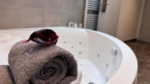 A bathroom with a large bathtub, a towel, and a flower. - Brit Hotel de Grignan (Vichy)