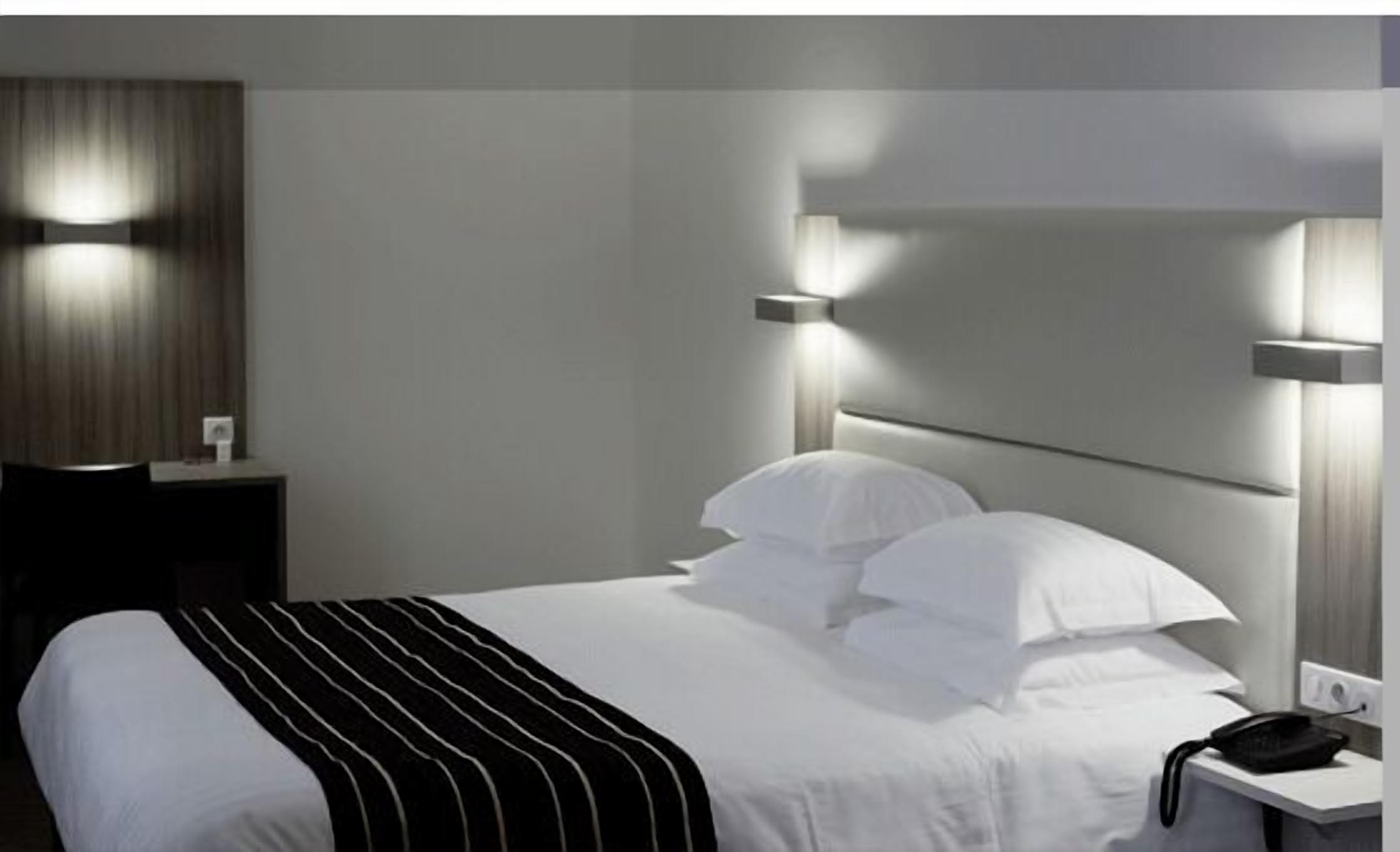 A hotel room with a large bed, a bedside table, and a nightstand.
