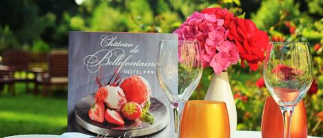 A table set with a menu, two wine glasses, a vase with flowers, and a plate of strawberries.