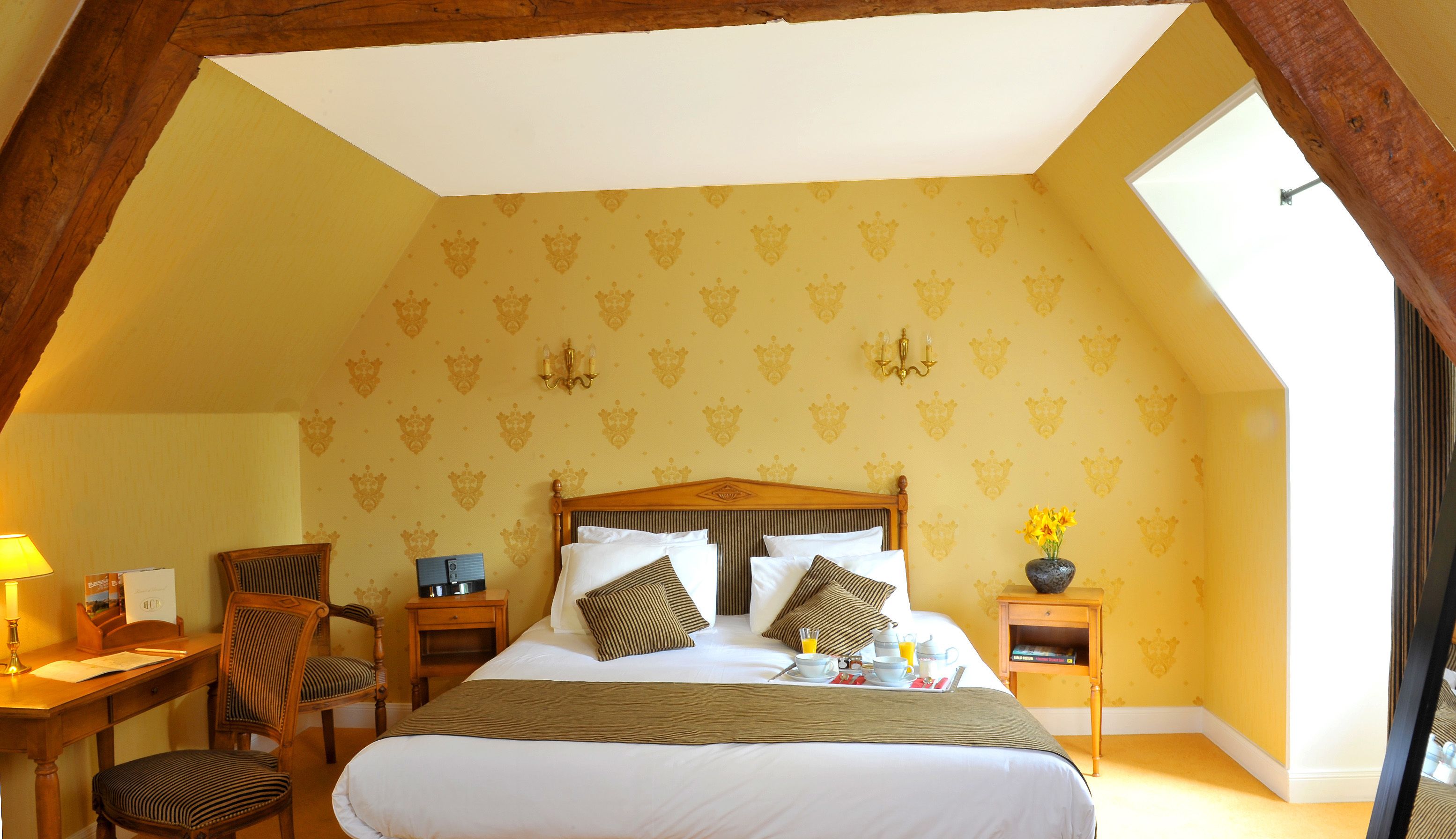 Un dormitorio con una cama grande, un escritorio con silla, una mesita con un florero y una ventana.