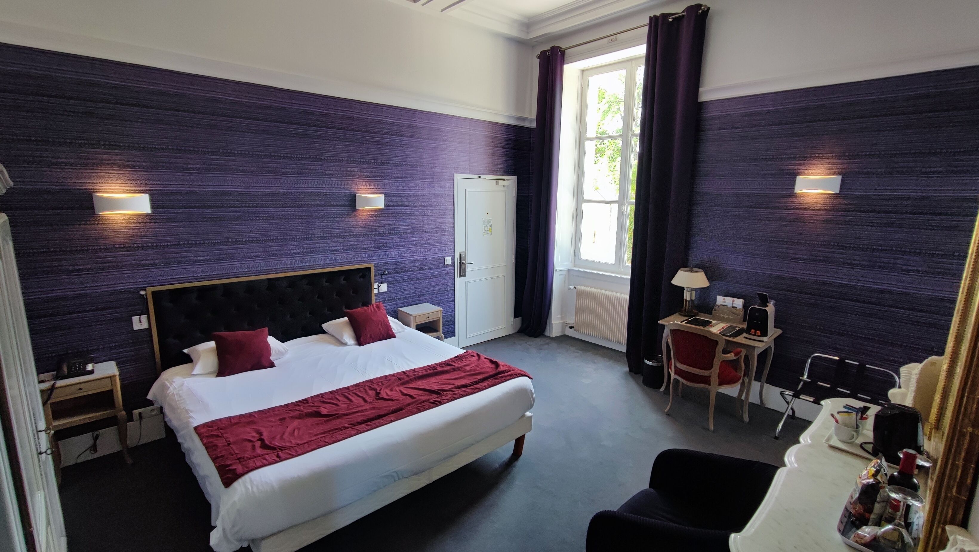 A hotel room with a large bed, a desk, a chair, and a small table.