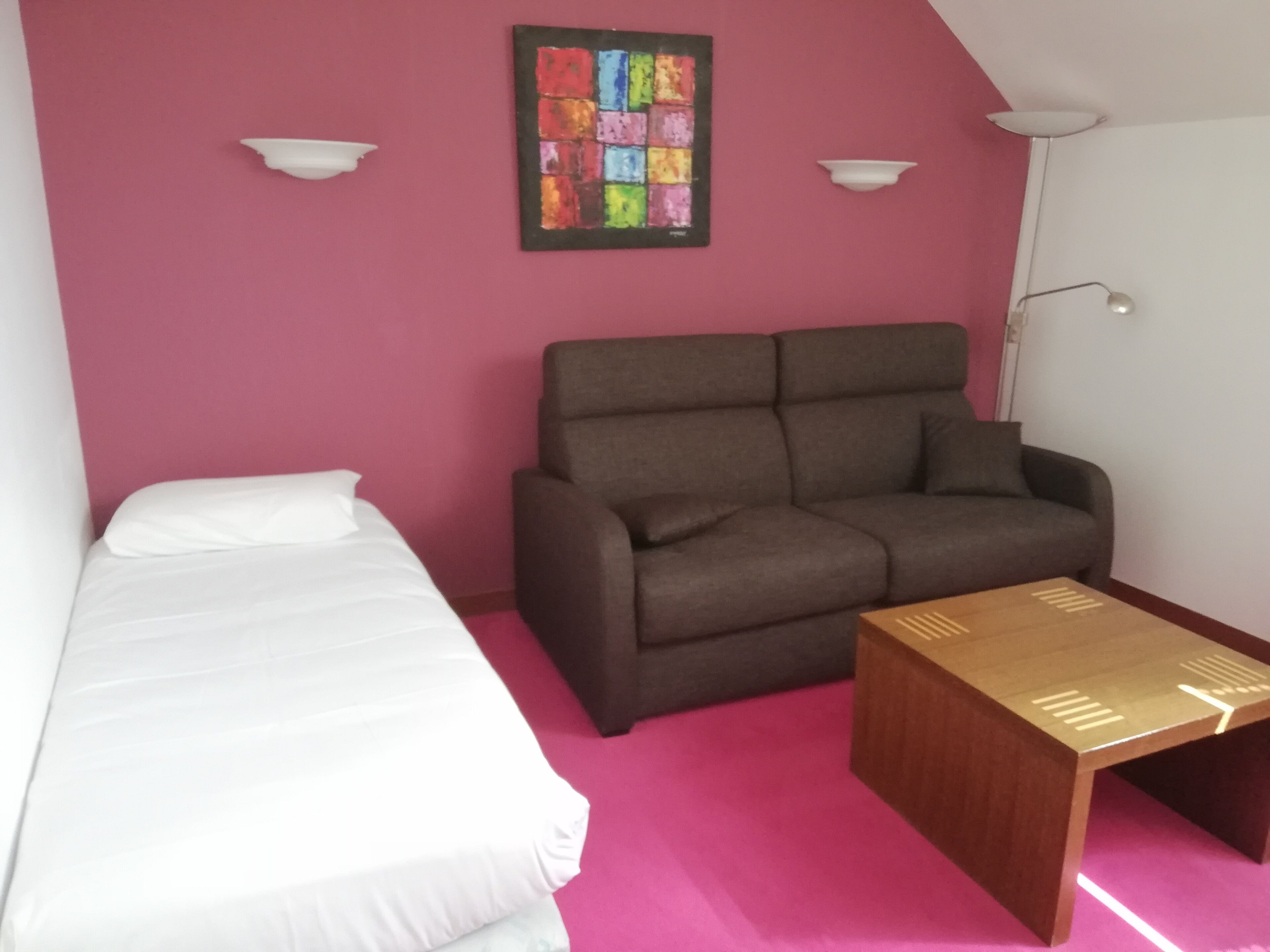 Une pièce comprenant un lit, un canapé, une petite table et une œuvre d’art colorée accrochée au mur.