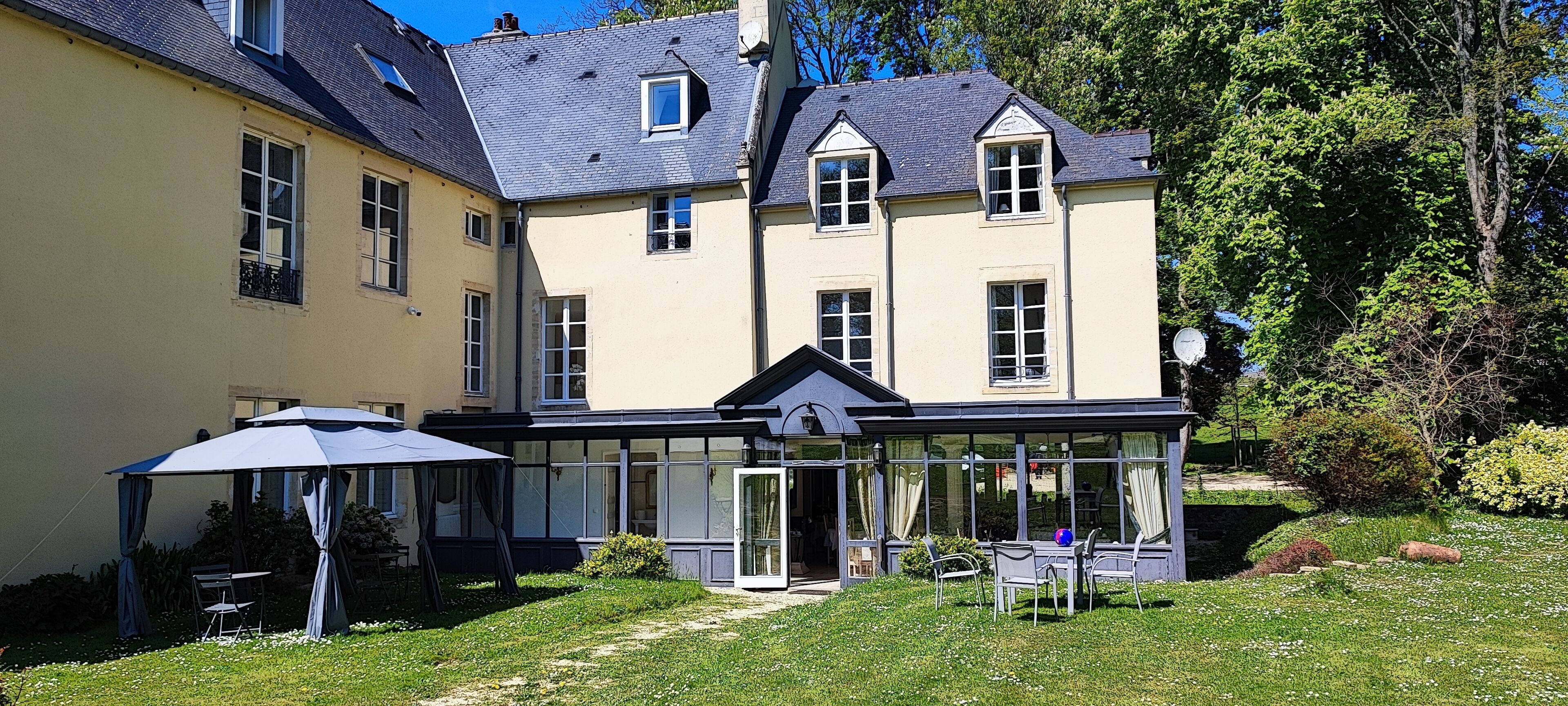 A two-story house with a glass conservatory, a covered patio, and a well-maintained garden.