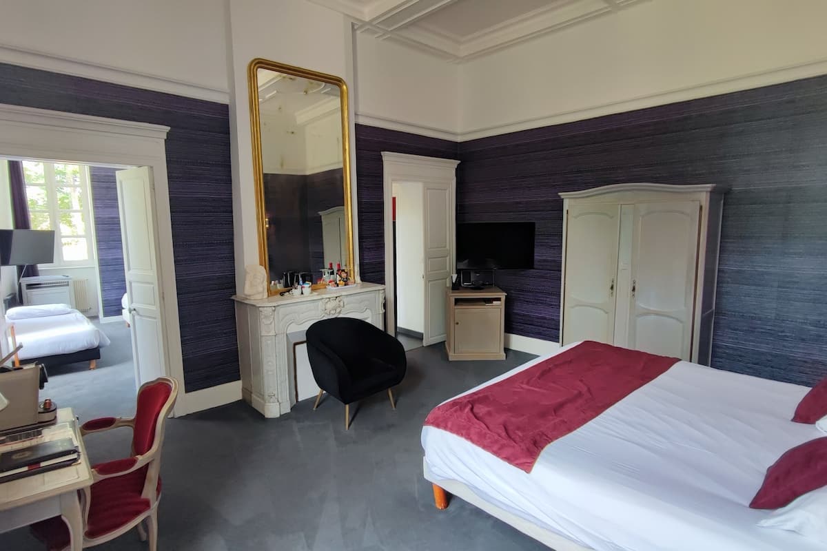 Habitación de hotel con cama, escritorio, silla, cómoda, televisor y armario.