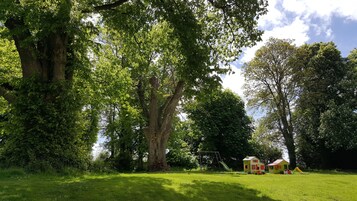A park with large trees, a playground, and two small houses.