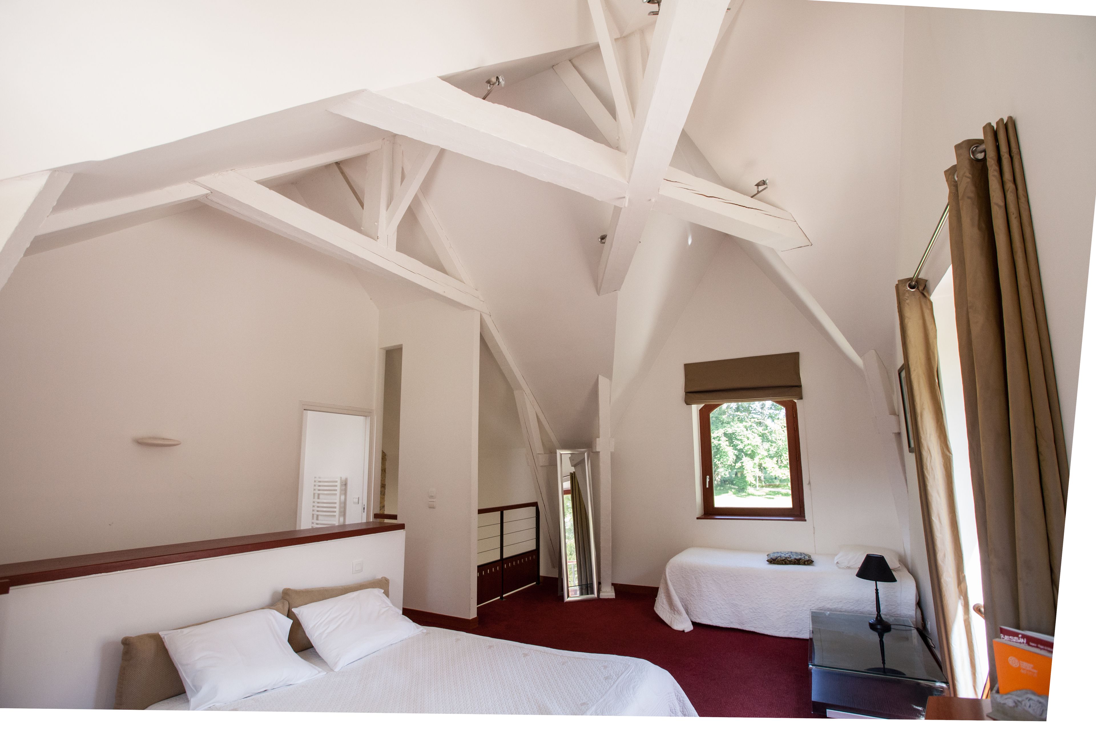 Ein Schlafzimmer mit zwei Betten, einem fensterförmigen Ausblick, einem Spiegel und einer Treppe zu einem weiteren Raum.