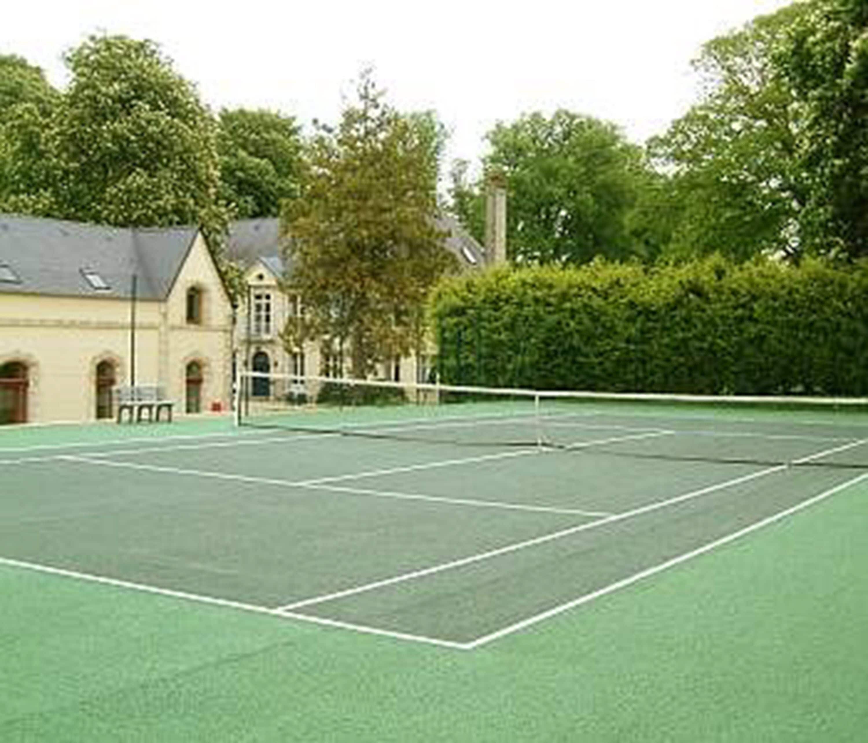 Een tennisbaan met een net, omringd door bomen en een gebouw met boogvensters.
