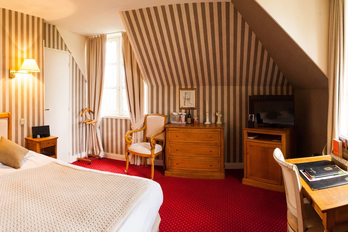 Una habitación de hotel con una cama grande, un escritorio, una silla, un televisor y una ventana con cortinas.