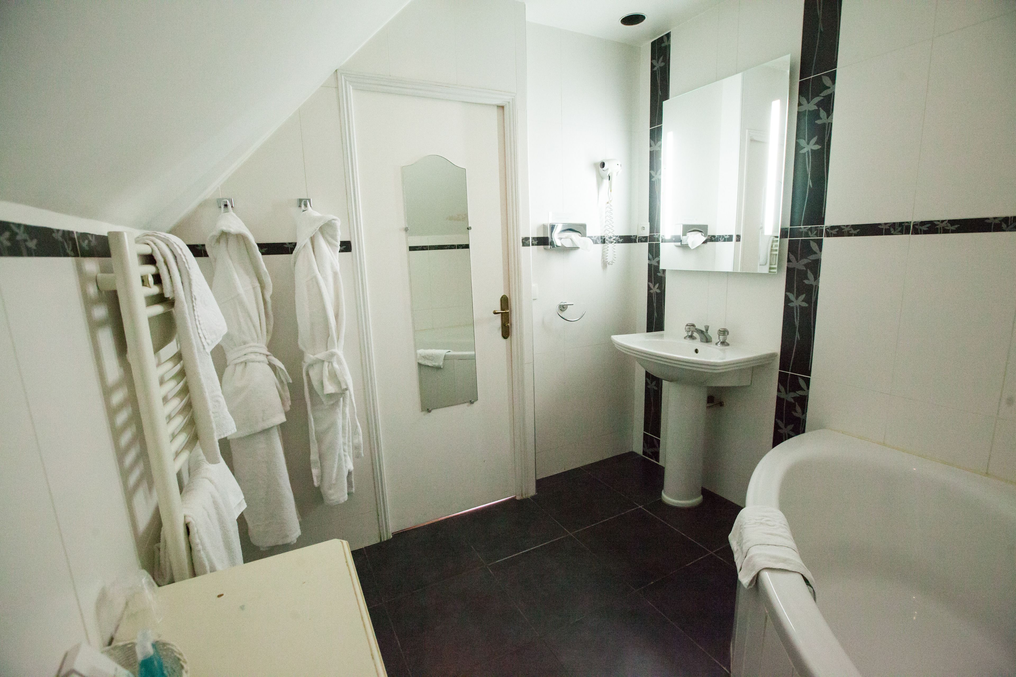 Un baño con bañera, lavamanos y espejo. Toallas colgadas en un perchero.