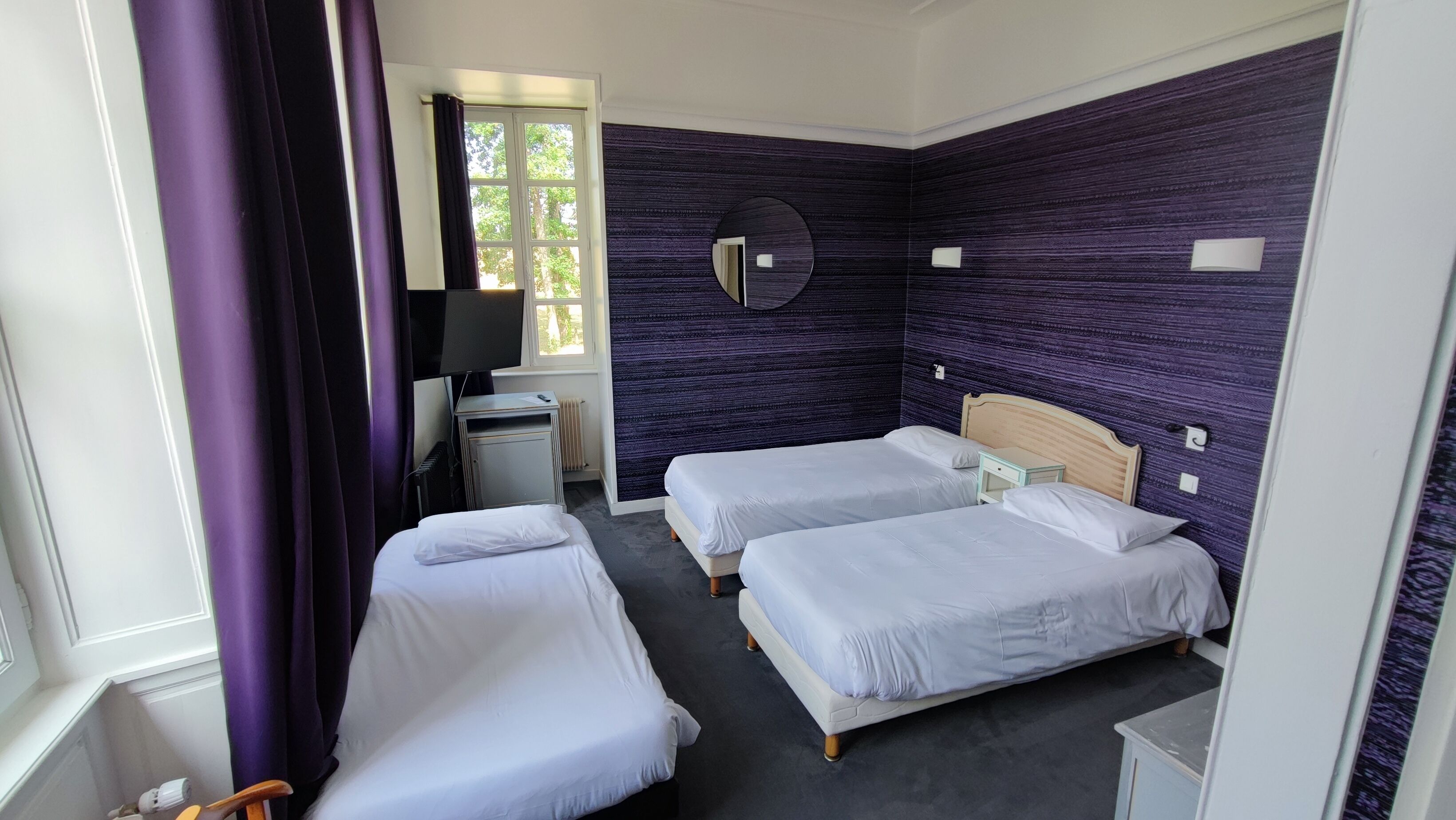 A hotel room with two single beds, a desk with a computer, a mirror, and a window with curtains.