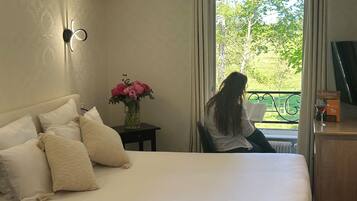 Une chambre à coucher avec un lit, une table de chevet ornée d’un vase de fleurs et une vue sur un balcon verdoyant.