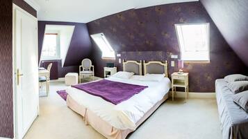 A bedroom with a large bed, a smaller sofa, a chair, and a desk. There are two windows providing natural light.