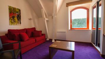 A room with a red sofa, a small table, a window with a view of trees, and a painting on the wall.