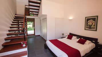 A bedroom with a bed, a wooden staircase, and a painting on the wall.