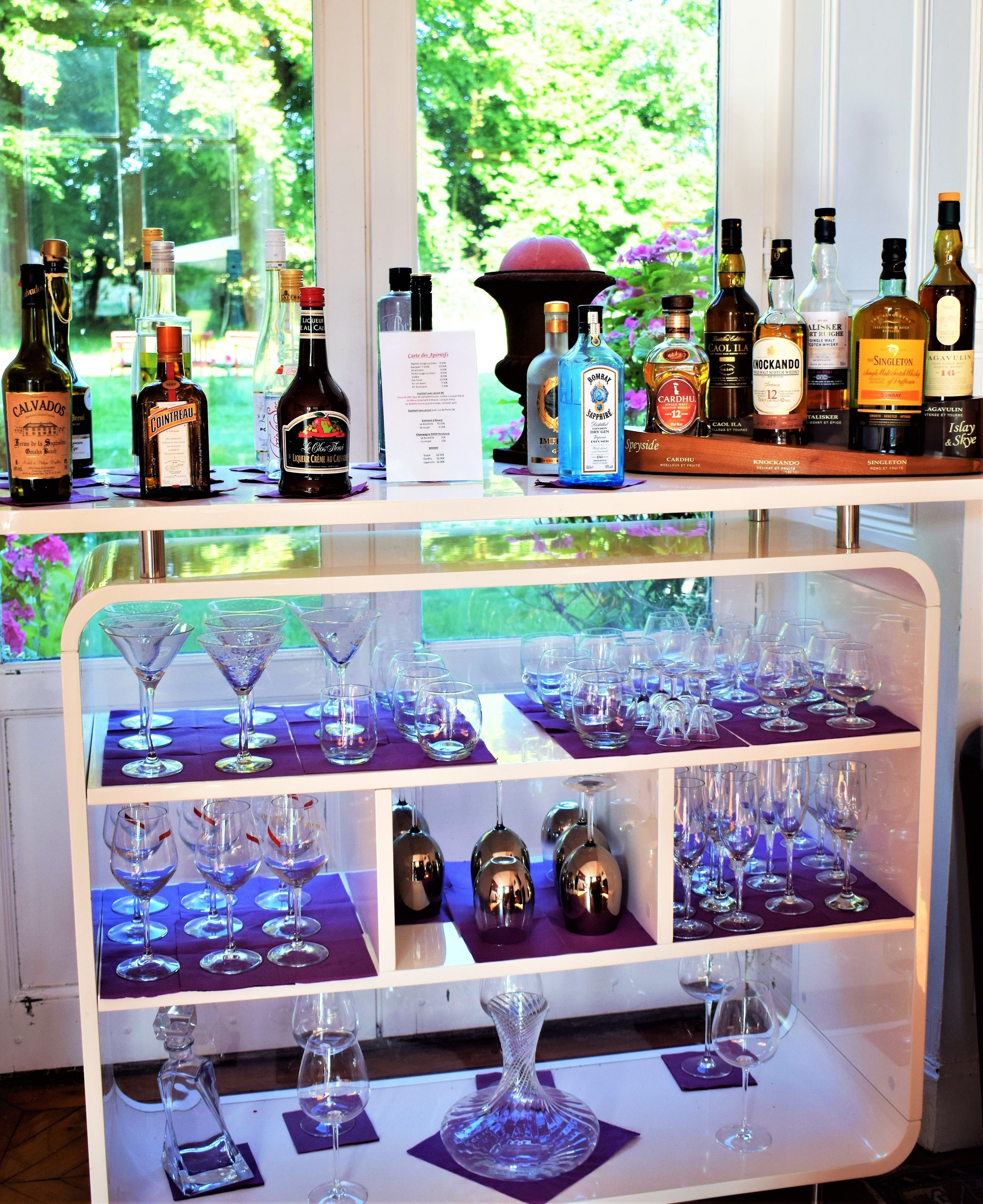 Zona de bar con una variedad de botellas de licores y múltiples copas de vino exhibidas en estantes.