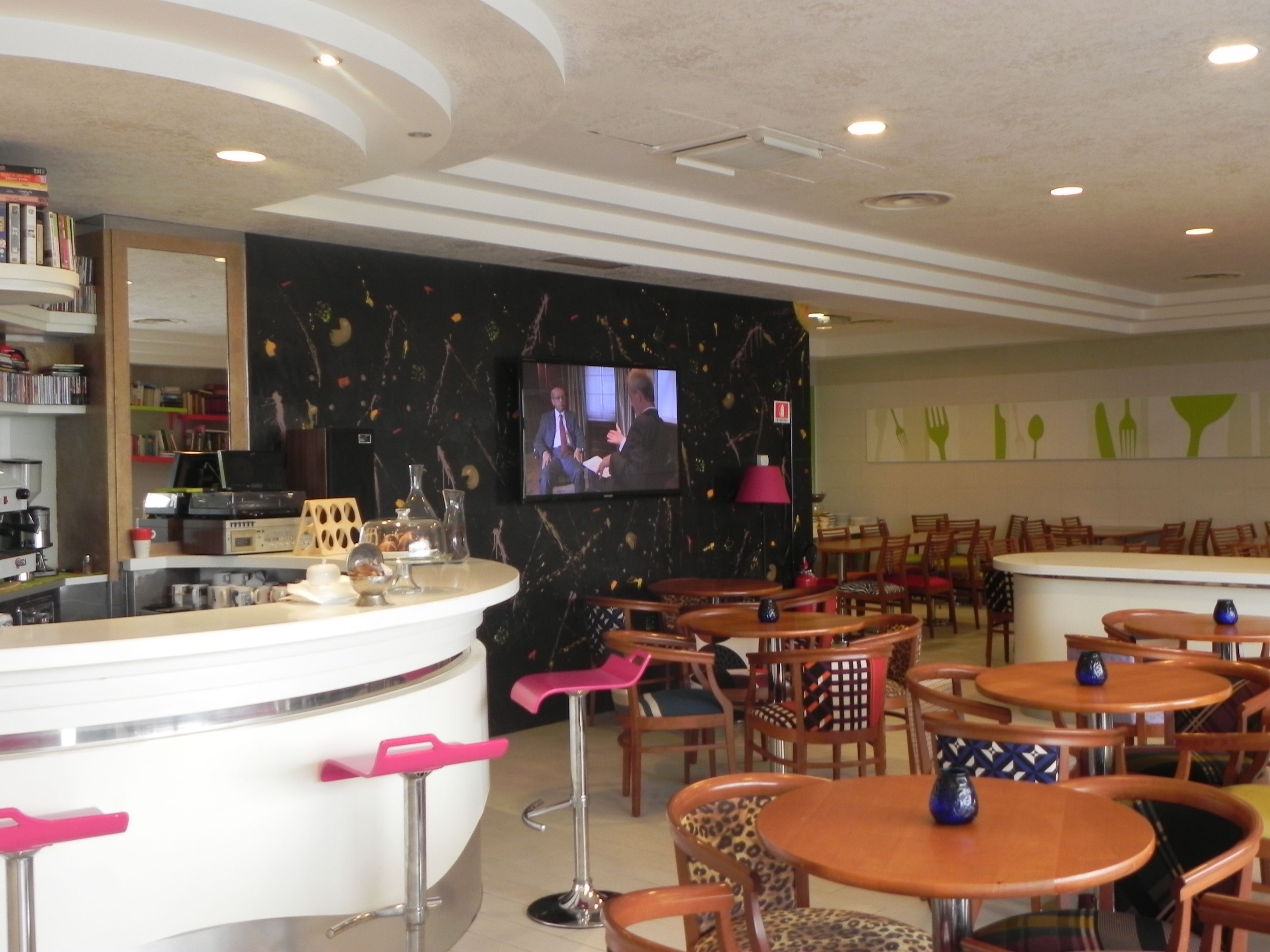 A modern restaurant interior with a bar area, multiple seating options, and a television screen displaying a program.