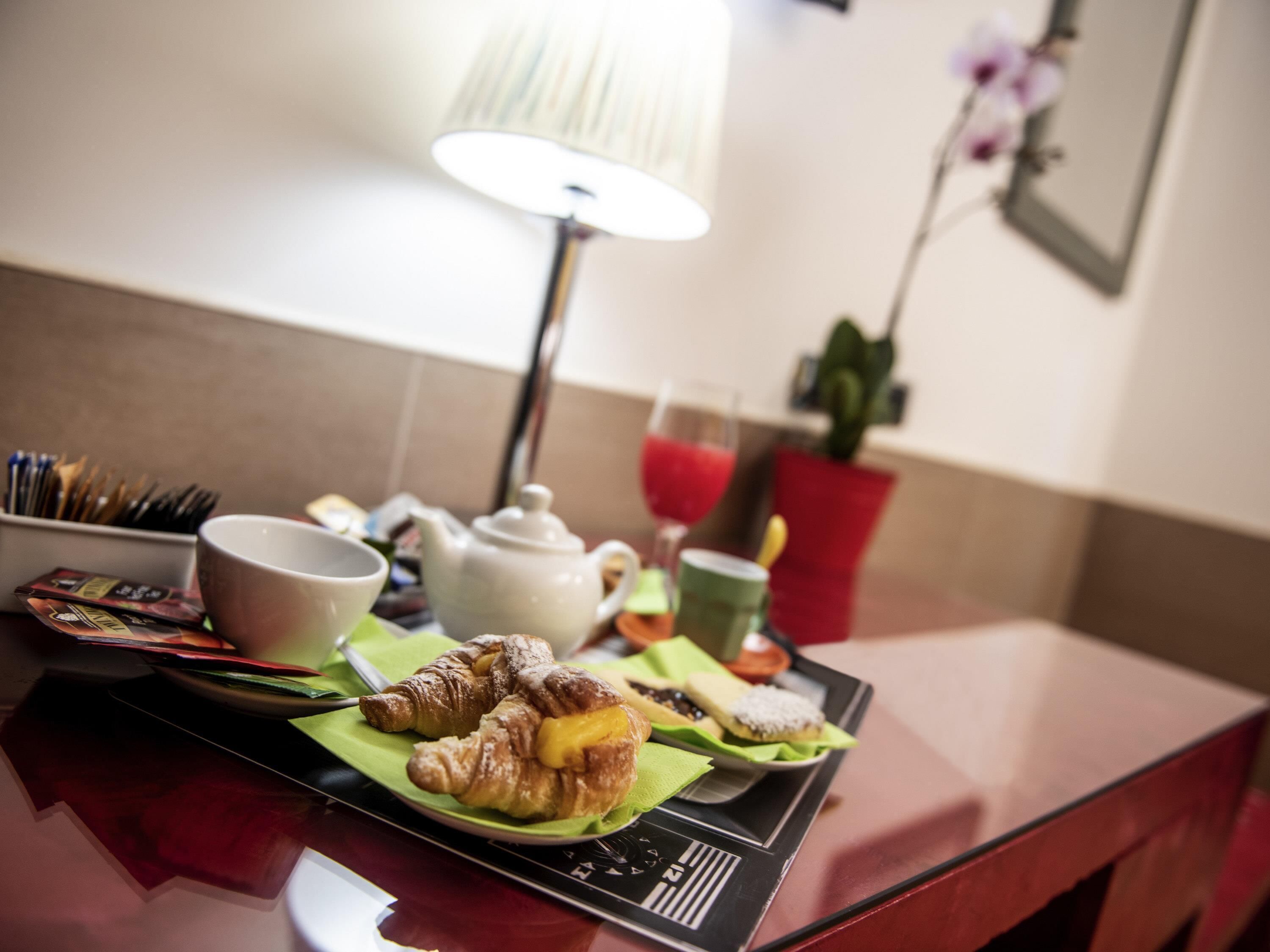 Una presentación para el desayuno con croissants, una tetera, una taza y jugo en una bandeja.