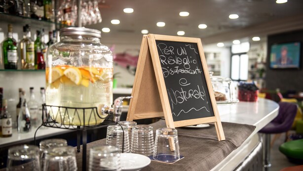 Un espace bar avec un grand bocal rempli d’une boisson aux fruits, un tableau noir servant de menu et divers verres et bouteilles.
