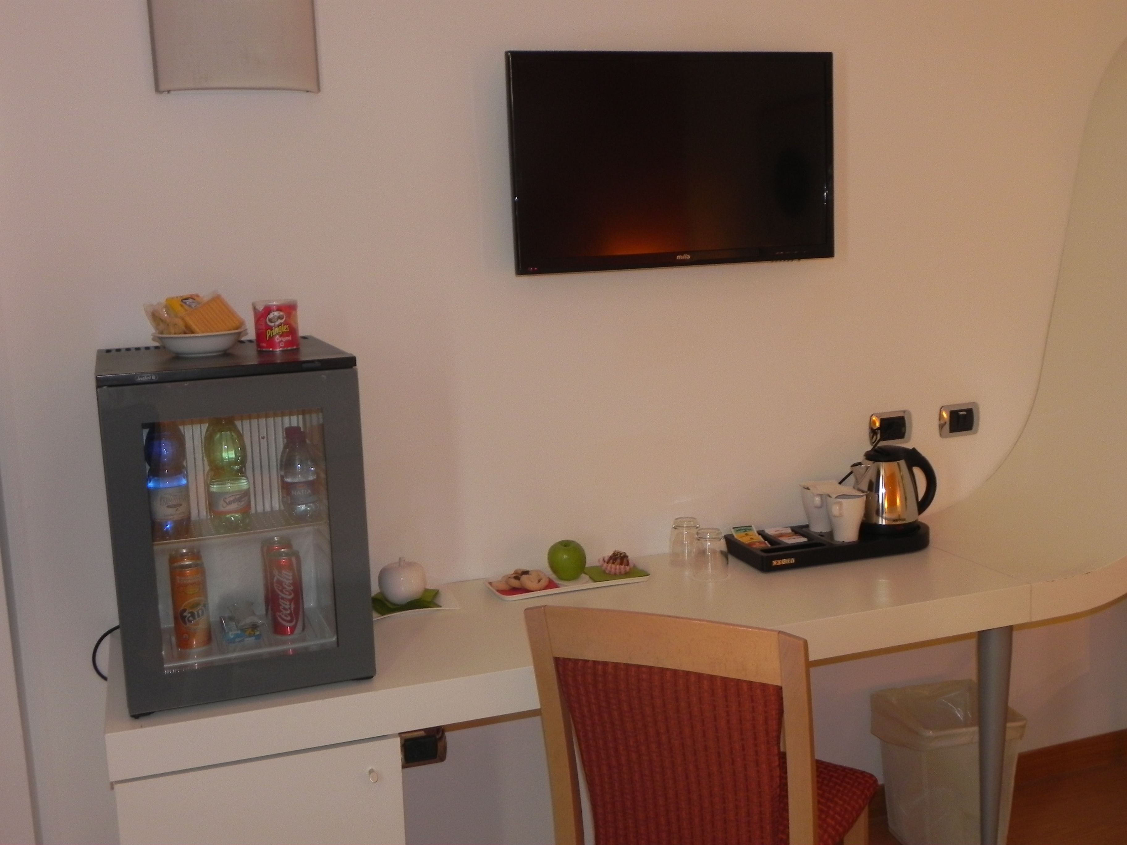 A kitchenette with a refrigerator, microwave, coffee maker, and a flat-screen TV mounted on the wall.