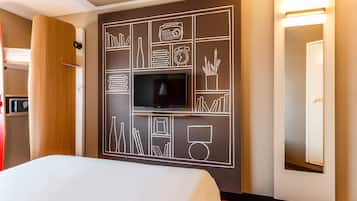 A hotel room with a bed, a television mounted on the wall, and a mirror.