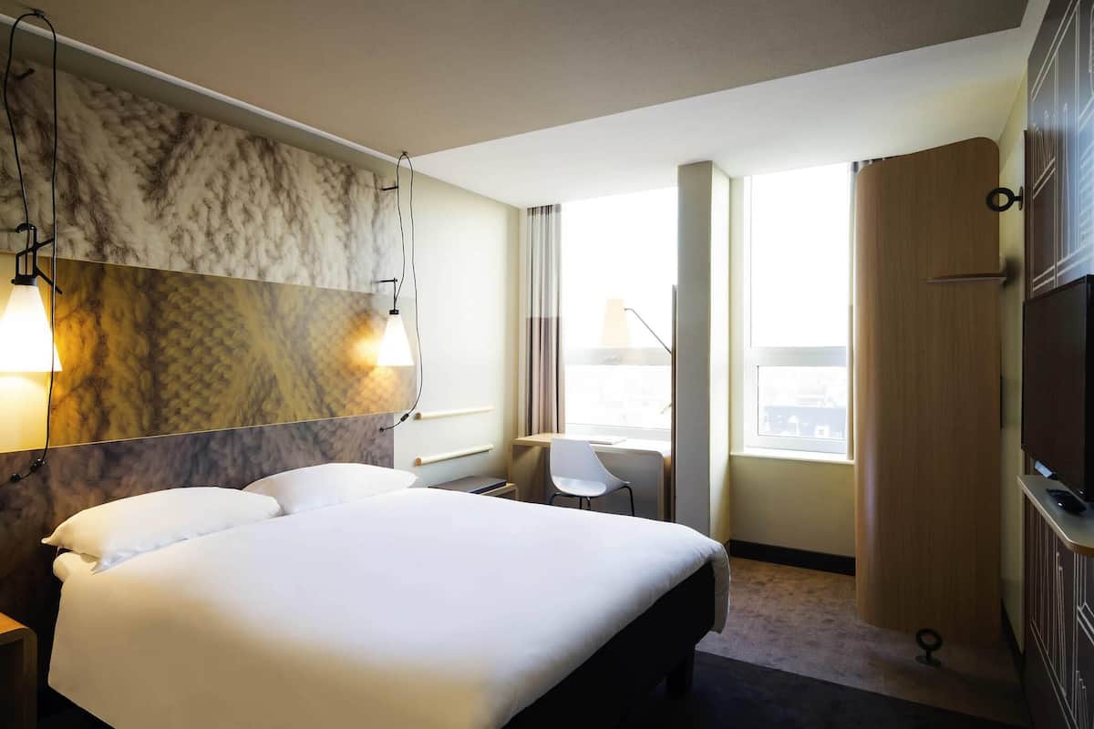 Una habitación de hotel con una cama grande, un escritorio, una silla, un armario y un televisor.