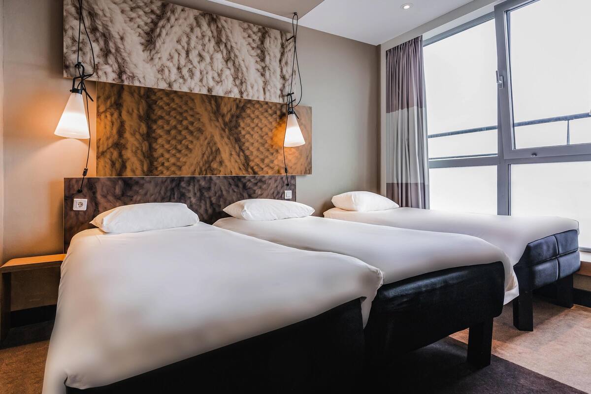 Ein Hotelzimmer mit zwei Betten, einer Marmorwand und einem großen Fenster mit Vorhängen.