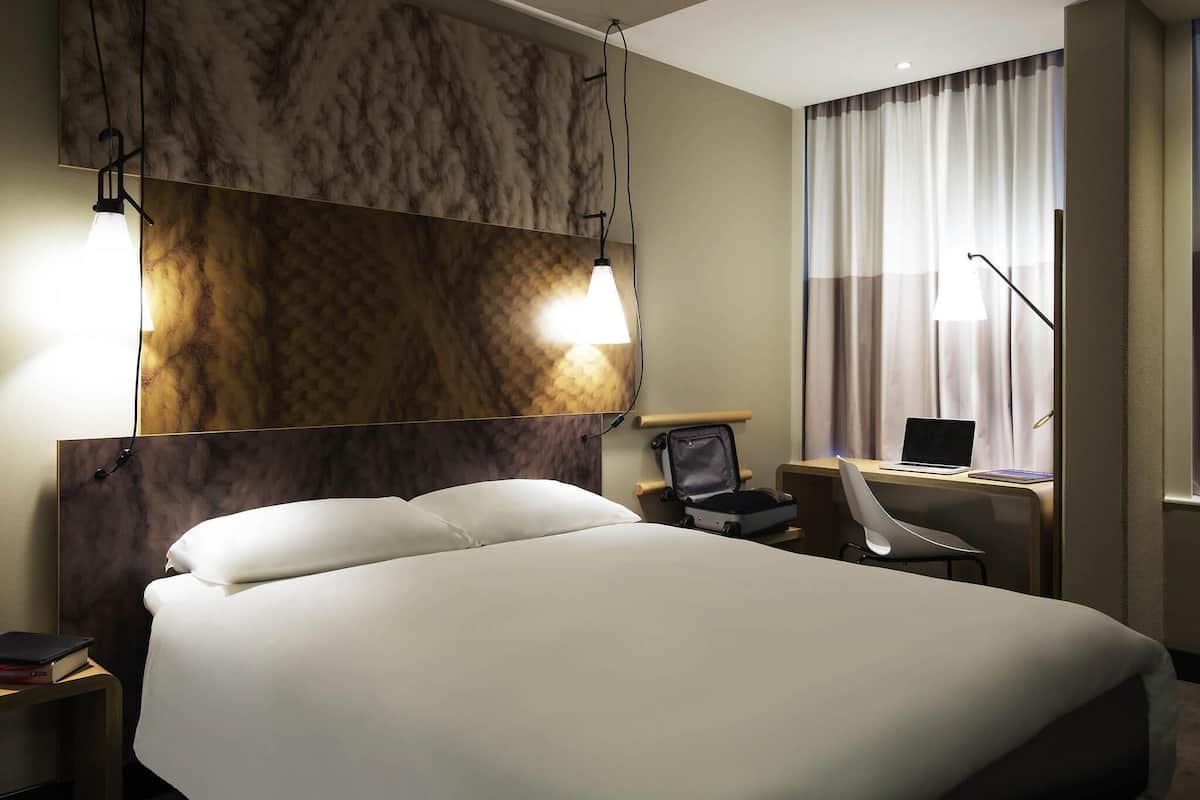 Ein Hotelzimmer mit einem großen Bett, zwei Nachttischlampen, einem Schreibtisch mit einem Laptop und einem Sessel.