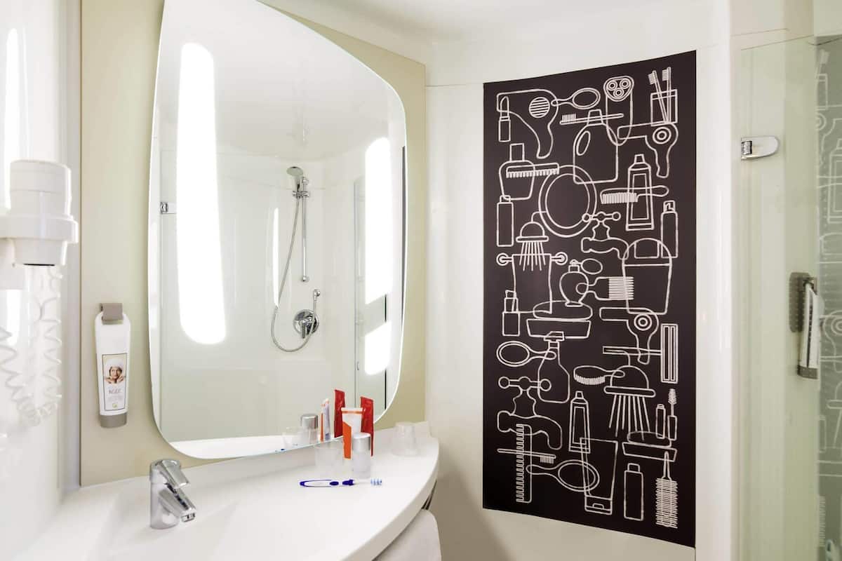 Ein Badezimmer mit einem weißen Waschbecken, einem Spiegel, einer Dusche und einem schwarzen Wandbild mit Badutensilien.