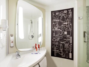 Un baño con un lavamanos blanco, un espejo, una ducha y una obra de arte en la pared negra que representa objetos de baño.