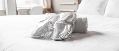 A neatly made bed with a pillow and a pair of shoes wrapped in plastic on it.