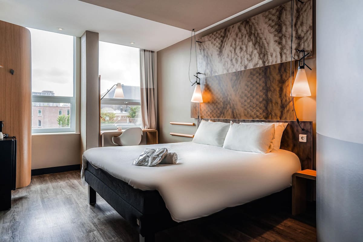 Ein modernes Hotelzimmer mit einem großen Bett, einem Schreibtisch und Blick auf die Stadt.