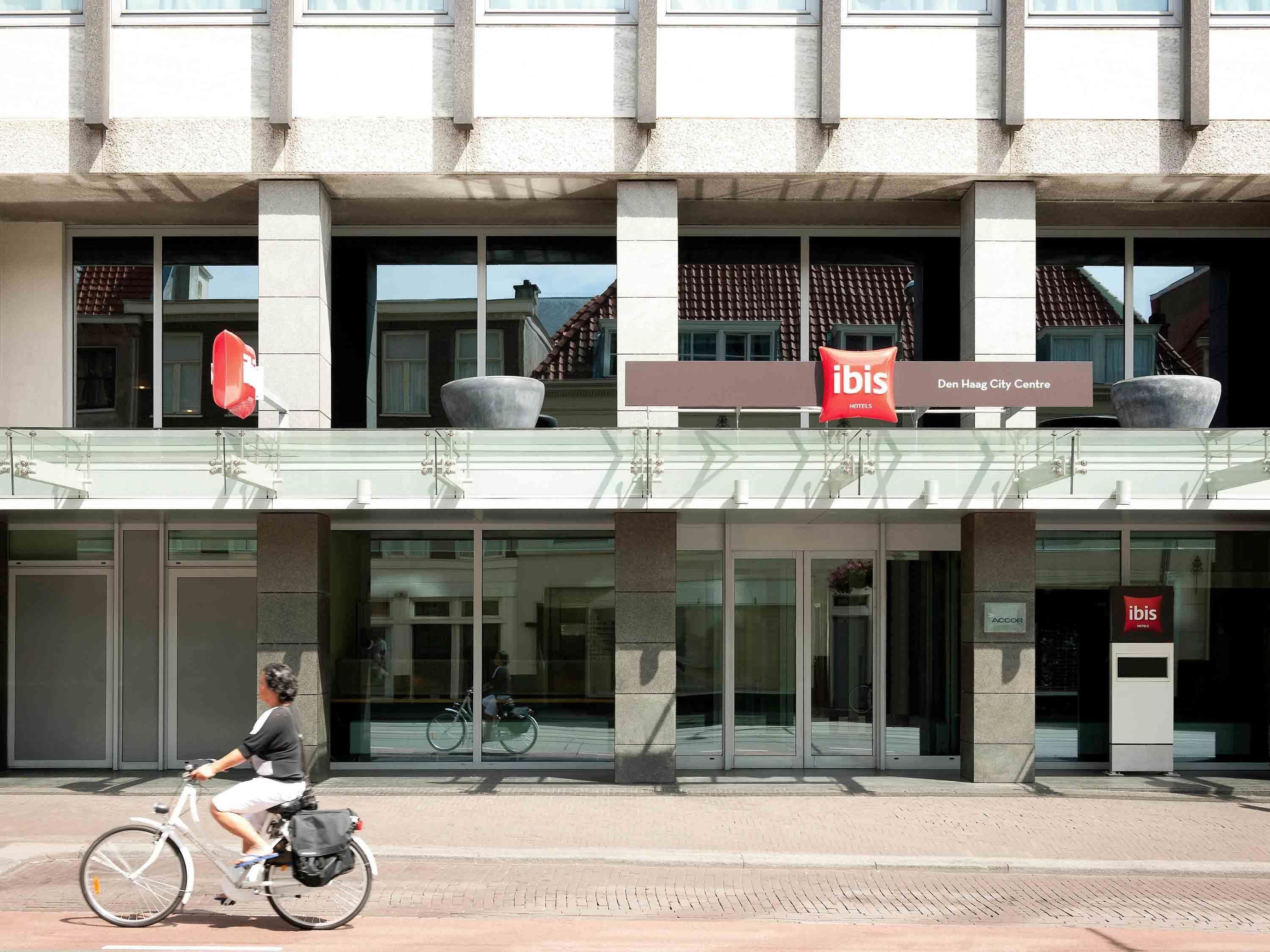 Un hotel moderno con fachada de vidrio, un aparcamiento para bicicletas y un llamativo letrero del hotel ibis.