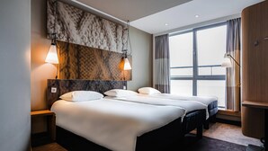 Een hotelkamer met twee bedden, een groot raam en uitzicht op de stad.