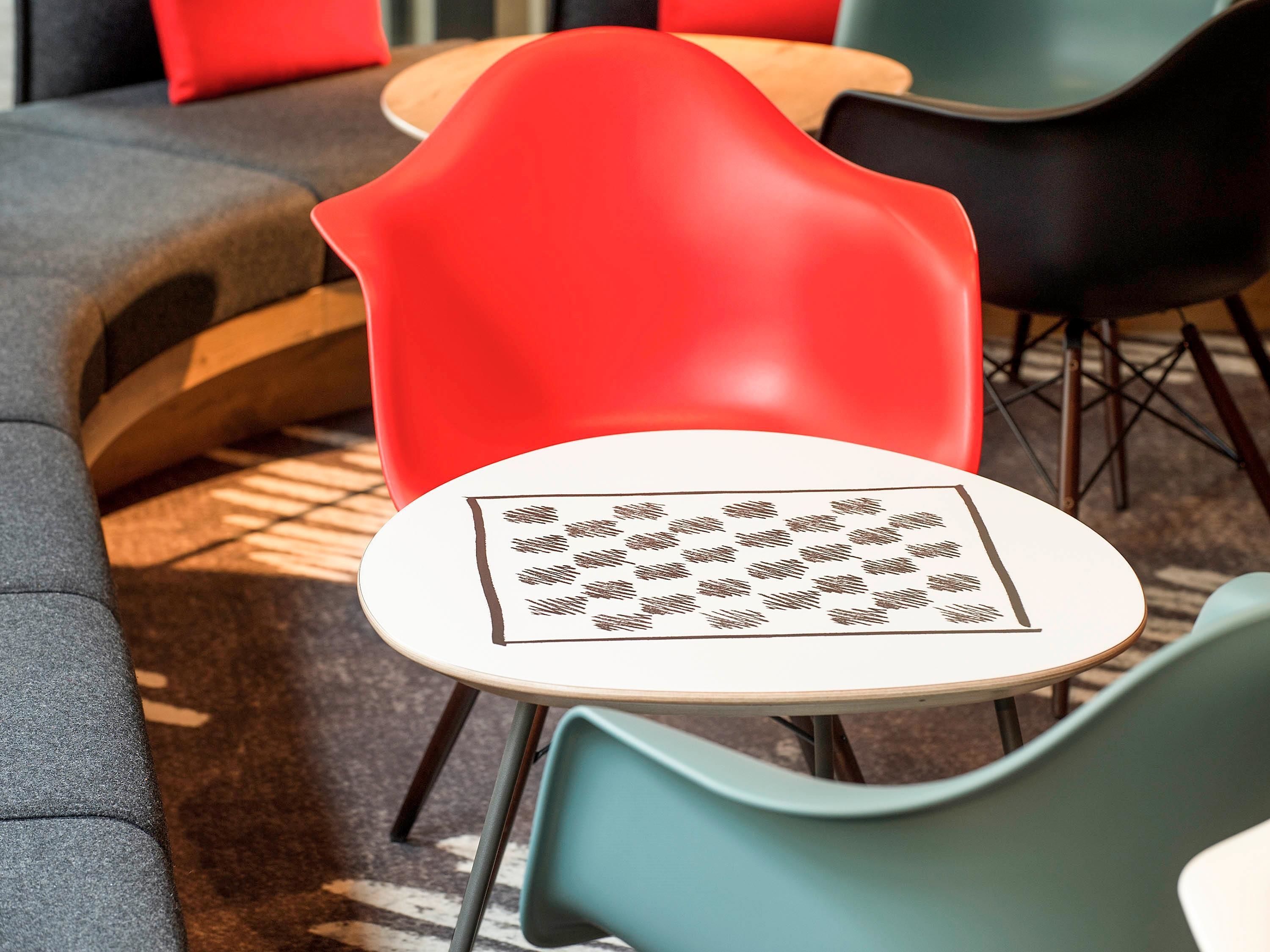 A modern seating area with a red chair, a round table with a patterned tablecloth, and a grey sofa.