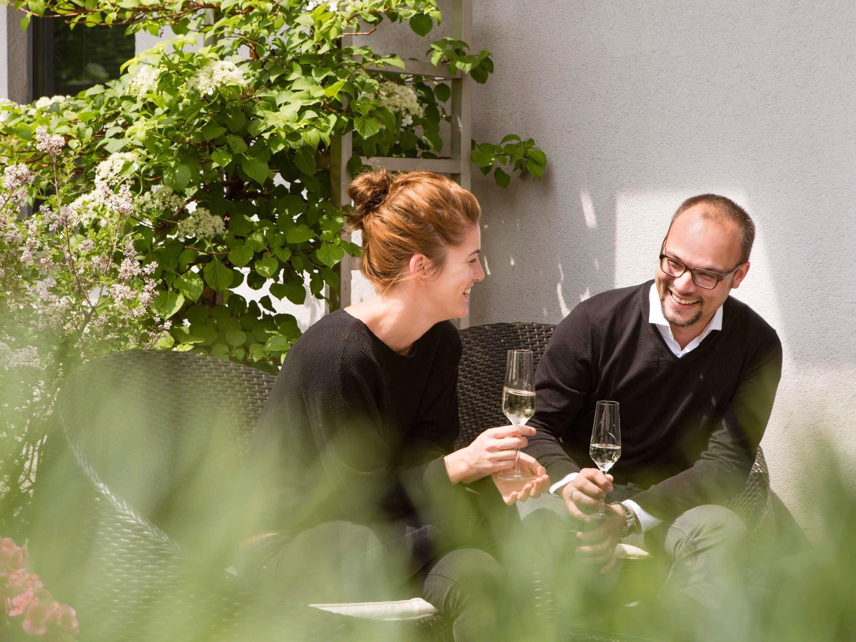 Due persone sedute su un divano di vimini all'aperto, che sorseggiano vino.
