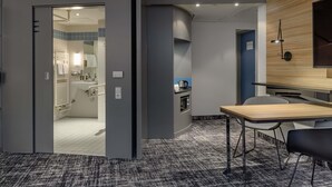 A modern hotel room with a grey and white color scheme, a wooden accent wall, a dining area with a table and chairs, and a kitchenette. - Novotel Suites Berlin City Potsdamer Platz (Berlin)