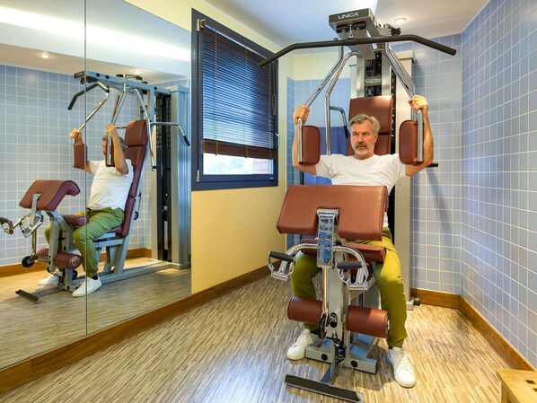 Un gimnasio con equipo de ejercicio, un espejo y una ventana con persianas.