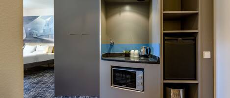 A modern hotel room with a kitchenette, a bed, and a bathroom.