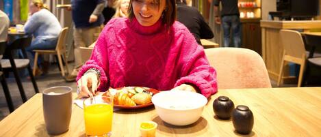 Una persona sentada a una mesa con comida, un vaso de jugo de naranja y un tazón.