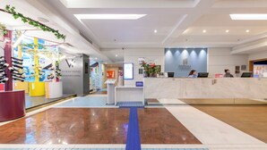 A modern hotel reception area with a blue tactile path for visually impaired guests, a shoe display, and a reception desk with computers and a sign indicating a waiting area. - Pestana Curitiba (Curitiba)