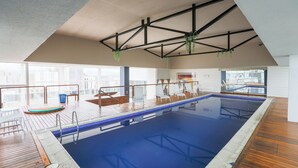 Una piscina interior con cubierta de madera, sillas de descanso y plantas colgantes.