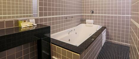 A modern bathroom with a large bathtub, a black countertop, and a tiled wall.