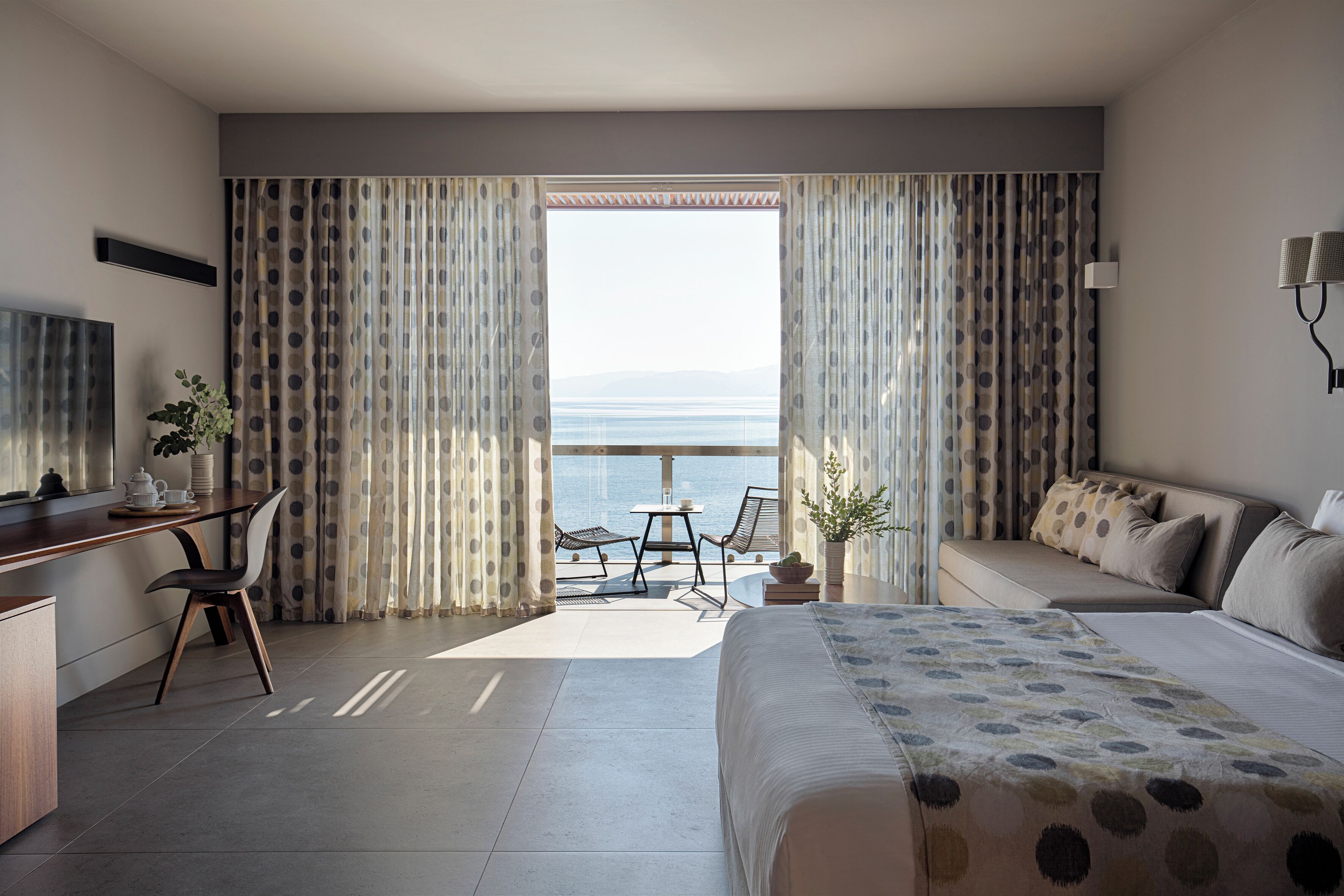 Habitación de hotel con una cama, un escritorio, una silla, un sofá y vista al mar.